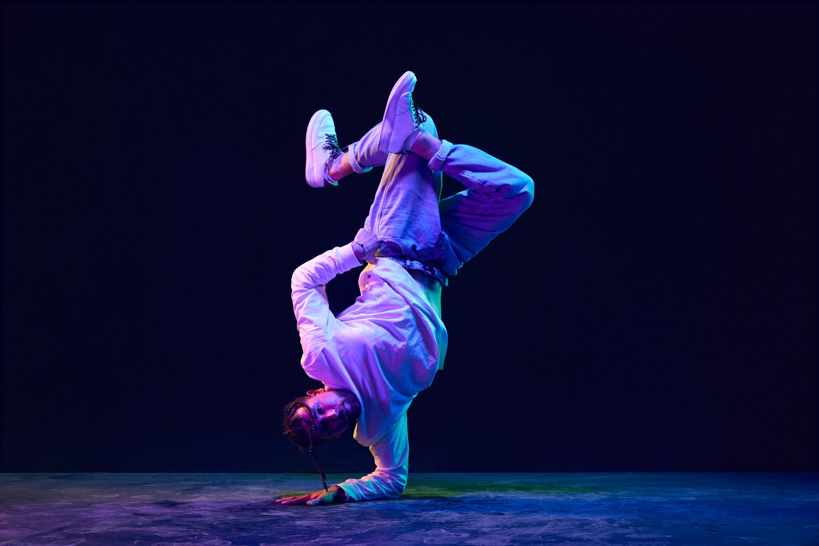 Trick. Artistic, sportive young man in sprotive clothes dancing breakdance, hip-hop against black studio background in neon light